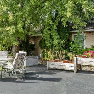 A cozy patio area with outdoor furniture surrounded by lush greenery and flower beds.