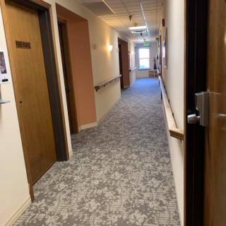 A long, carpeted hallway with multiple doors and overhead lighting.