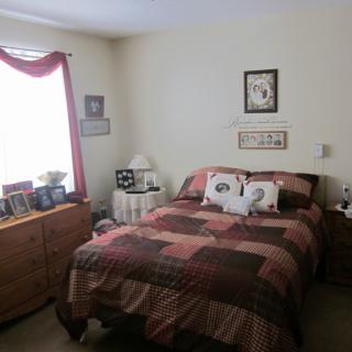 A cozy bedroom with a bed, dresser, and window with red curtains.