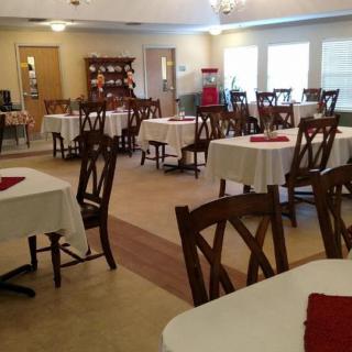An empty dining room with tables and chairs neatly arranged, featuring white tablecloths and red napkins.