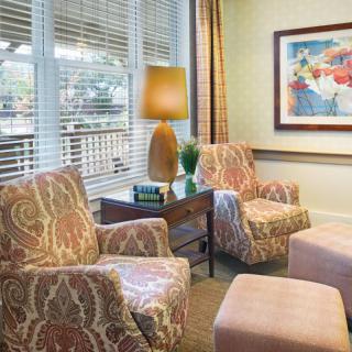 A cozy living room with patterned armchairs, a lamp, and a colorful painting on the wall.