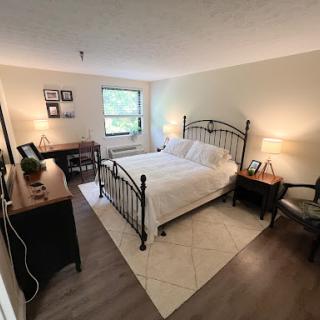 A cozy and well-lit bedroom featuring a metal bed frame, desk, and comfortable seating.