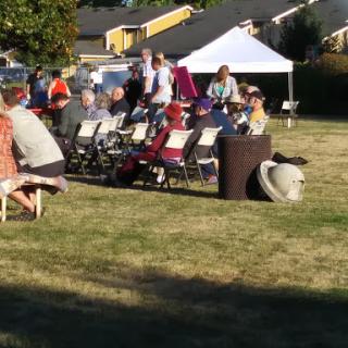 A gathering of people seated outdoors, enjoying a daytime event under a tent.