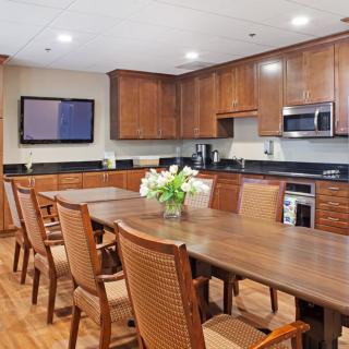 A modern kitchen and dining area featuring wooden cabinets, a large table with chairs, and decorative flowers.
