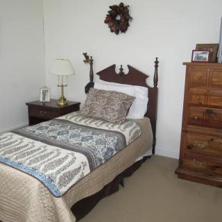 A cozy bedroom with a single bed adorned with printed quilted bedding, a nightstand with a lamp, and a wooden dresser.