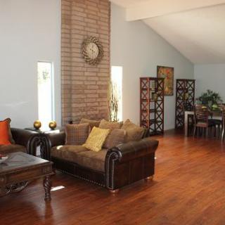 A spacious living room with wooden flooring, featuring cozy sofas and a brick accent wall.