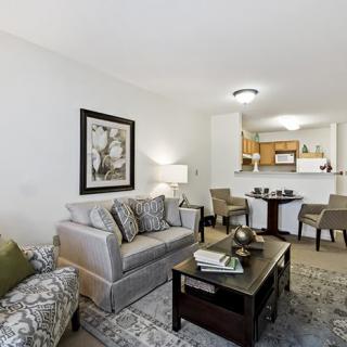 A modern living room with a sofa, coffee table, and adjacent dining area leading to the kitchen.