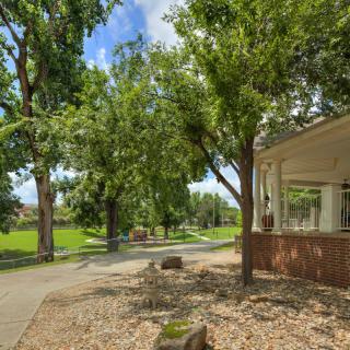A tranquil park scene with a pathway bordered by lush green trees and a building on the right.
