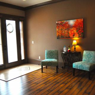 A cozy waiting room with teal chairs, a small table with a lamp, and colorful artwork on the wall.