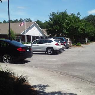 A view of a parking lot with several vehicles and a building in the background on a sunny day.