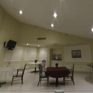 A spacious room with a table and chairs, featuring overhead lighting and a wall-mounted television.