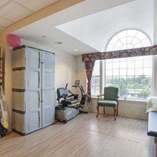 A well-lit exercise room featuring fitness equipment and seating next to a large window.