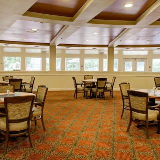 A spacious dining area with multiple tables and chairs, featuring large windows and patterned carpet.