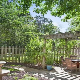 A tranquil garden with a pergola and outdoor seating area, surrounded by lush greenery.