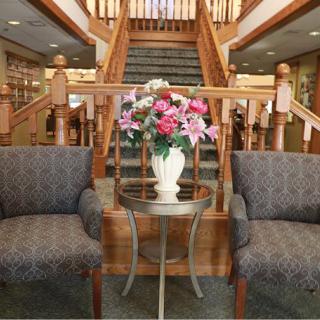 A lobby area with two chairs and a table with a flower vase, set in front of a wooden staircase.