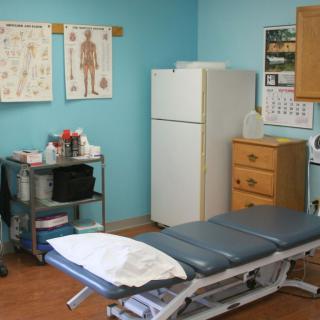 A medical examination room with a treatment table, anatomical charts, and various medical supplies.