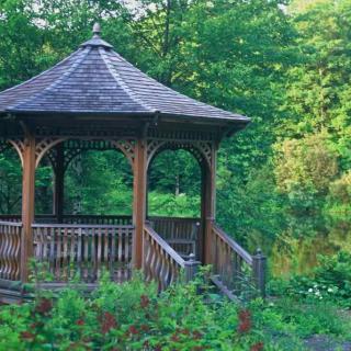 A wooden gazebo surrounded by lush greenery in a garden setting.