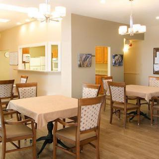 A cozy dining room with several tables and chairs, warm lighting, and a glimpse of the kitchen area.
