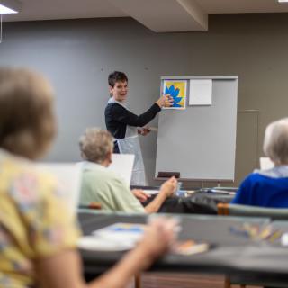 An art instructor teaches a painting class to senior citizens.