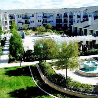 A modern apartment complex featuring a courtyard with a pool and fountain surrounded by lush landscaping.