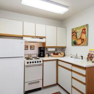 A small kitchen with white cabinets, a refrigerator, a stove, and colorful rooster wall art.