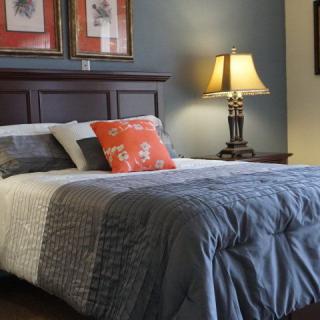 A cozy bedroom featuring a neatly made bed with a stylish blue comforter, decorative pillows, and a bedside lamp.