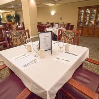 An elegantly set dining table in a restaurant interior, featuring neatly arranged cutlery and a menu at the center.