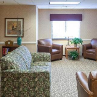 A cozy waiting room featuring a sofa, two armchairs, a small table with a plant, and a painting on the wall.