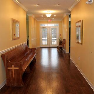 A hallway with a wooden bench featuring a cross, leading to glass double doors.
