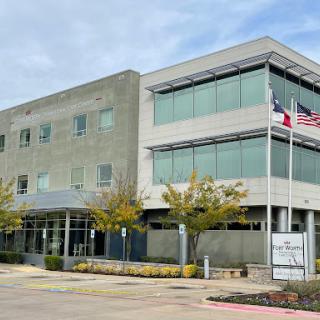 A modern office building featuring large windows and landscaped surroundings.
