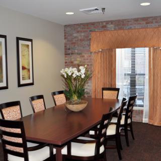 A stylish dining room with a long wooden table, cushioned chairs, and decorative elements including framed wall art and a flower arrangement.