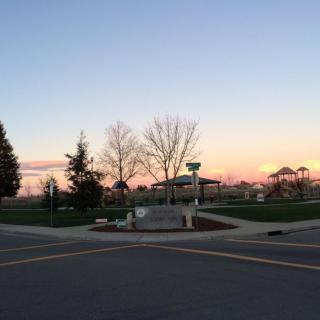 A scenic view of a park at sunset, featuring bare trees and a pavilion under a colorful sky.