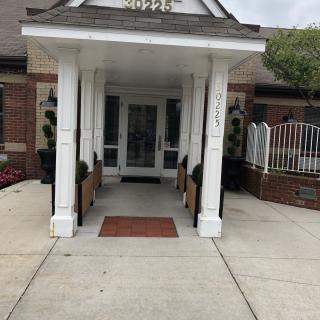 The entrance to a brick building with white columns and potted plants.