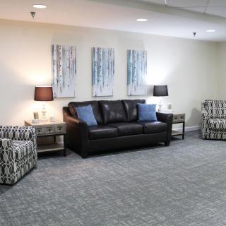 A well-furnished living room with a black sofa, patterned armchairs, and artwork on the wall.