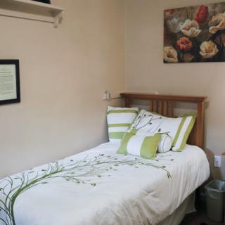 A cozy bedroom with a single bed adorned with green and white bedding, featuring floral artwork on the wall.
