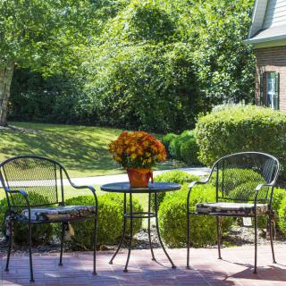 A peaceful patio setting with two chairs and a table adorned with flowers, overlooking a lush garden.