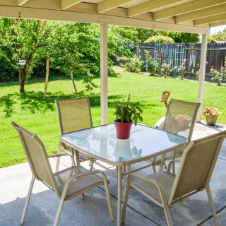 A cozy patio setup with a glass table and four chairs overlooking a lush green backyard.