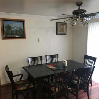 A cozy dining room with a wooden table and chairs, featuring a ceiling fan and wall paintings.