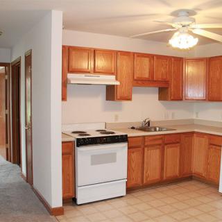 A cozy apartment kitchen with wooden cabinets and a ceiling fan.