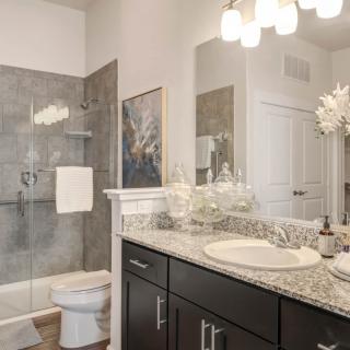 A modern bathroom featuring a granite countertop, glass-enclosed shower, and elegant lighting.