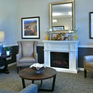 A cozy living room featuring a fireplace with a mirror above, flanked by artwork and armchairs, and centered around a wooden coffee table.