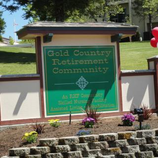Entrance sign for Gold Country Retirement Community surrounded by landscaping and flowers.