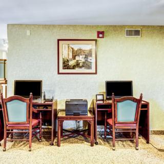 A small office area with two desks each equipped with computers and chairs, featuring a framed painting on the wall.