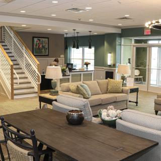 A modern living room with comfortable sofas, a large wooden table, and a staircase leading to the upper level.