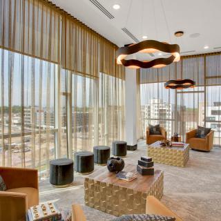 A modern lounge with large windows offering a city view, featuring contemporary seating and decor.