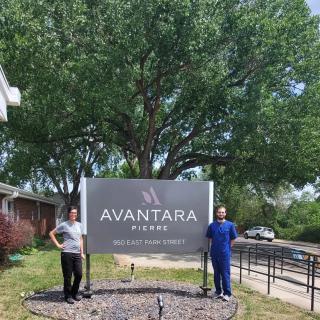 Two individuals stand beside the Avantara Park Ridge sign outdoors.