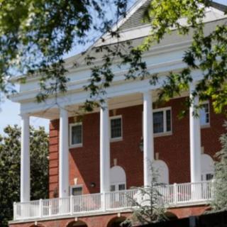 A brick building with white columns surrounded by trees.