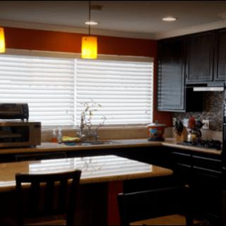 A modern kitchen with dark cabinets, a light-colored countertop, and various appliances under warm lighting.