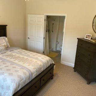 A cozy bedroom featuring a neatly made bed with patterned bedding, a wooden dresser, and an en suite bathroom doorway.