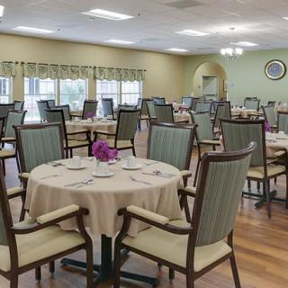 A neatly arranged dining room with round tables and upholstered chairs.
